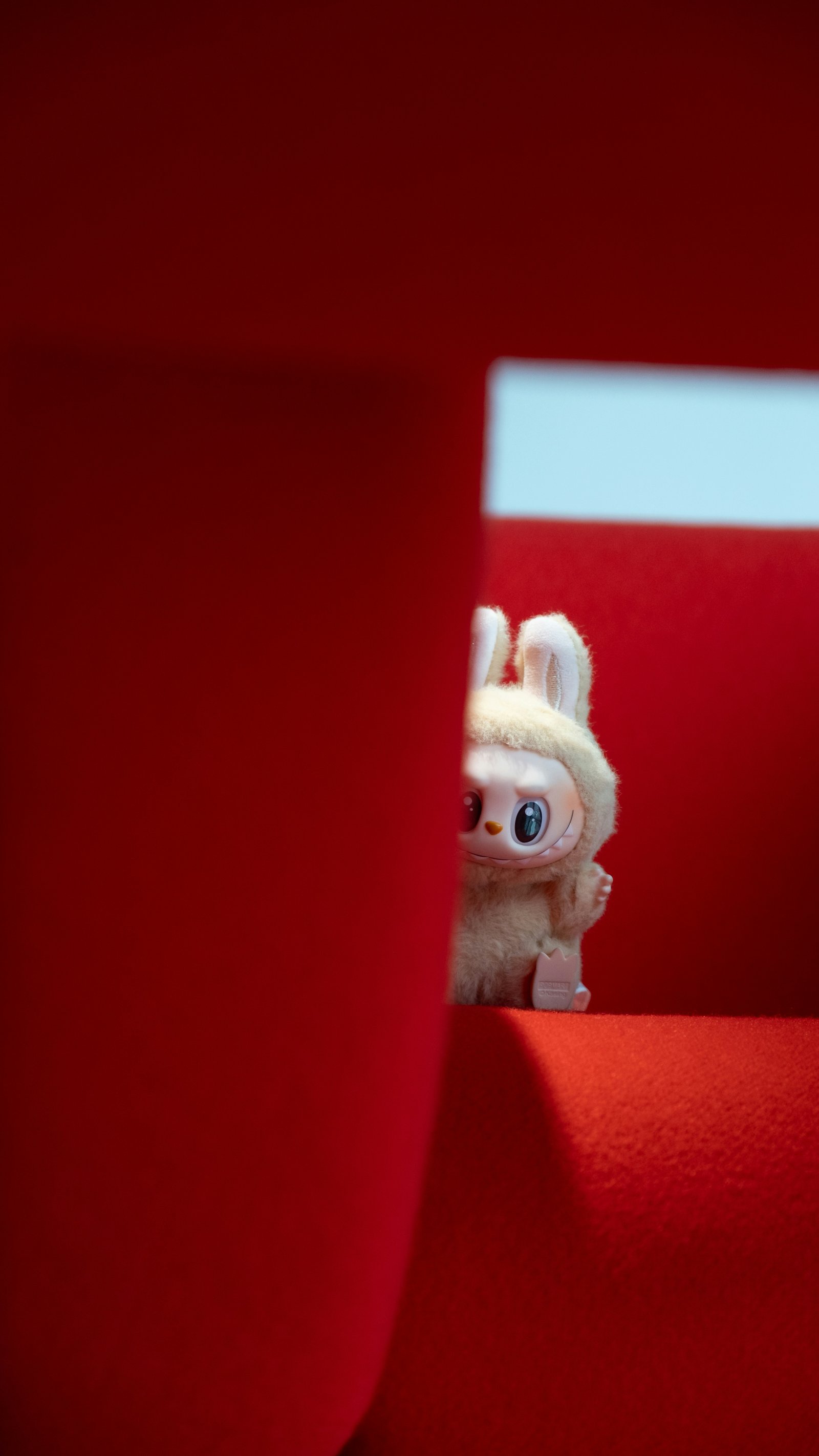 Labubu plush peeking from behind a red couch, echoing the whimsical seating theme of the Have a Seat series.
